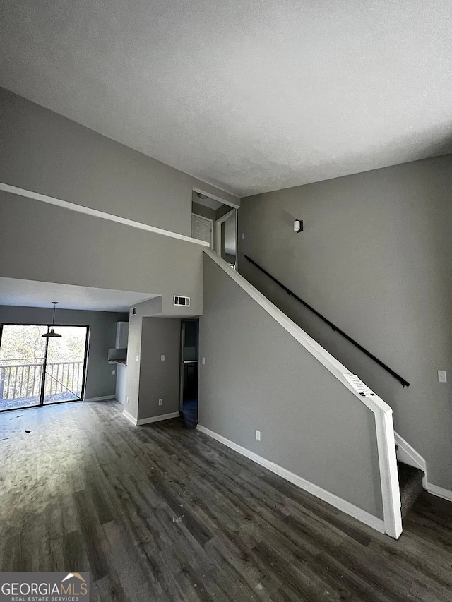 unfurnished living room with visible vents, a textured ceiling, wood finished floors, stairway, and baseboards