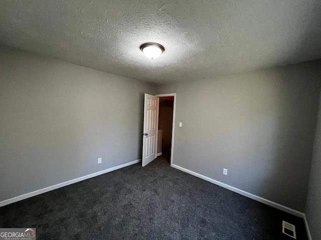 unfurnished room featuring visible vents, a textured ceiling, baseboards, and dark colored carpet