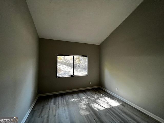 empty room featuring vaulted ceiling, baseboards, and wood finished floors