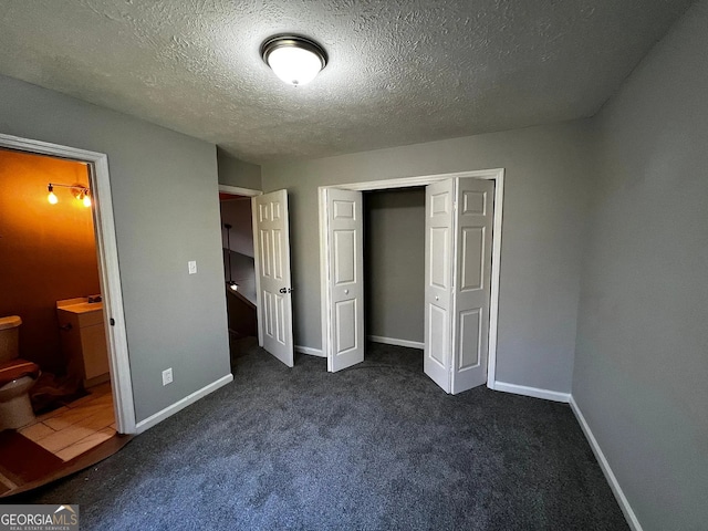 unfurnished bedroom featuring ensuite bathroom, a textured ceiling, dark carpet, a closet, and baseboards