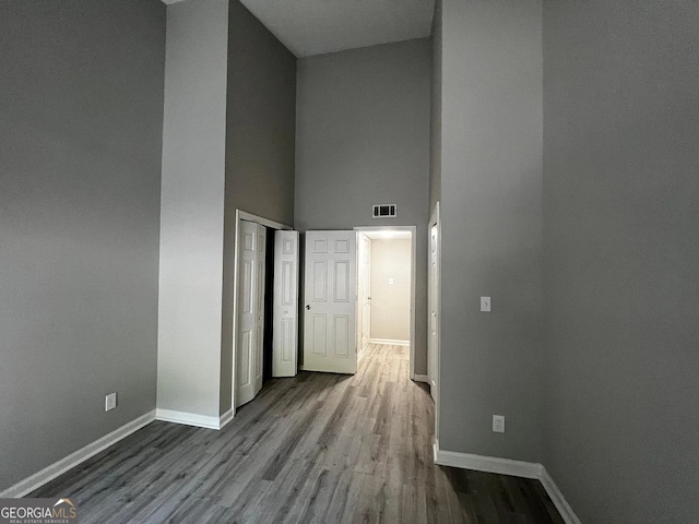 interior space with visible vents, baseboards, wood finished floors, and a towering ceiling