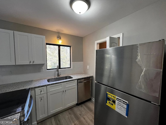 kitchen featuring a sink, light stone counters, tasteful backsplash, wood finished floors, and appliances with stainless steel finishes