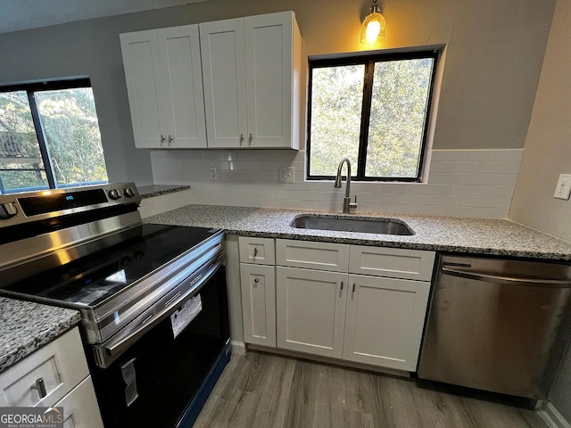 kitchen featuring light wood-style flooring, a sink, backsplash, appliances with stainless steel finishes, and light stone countertops