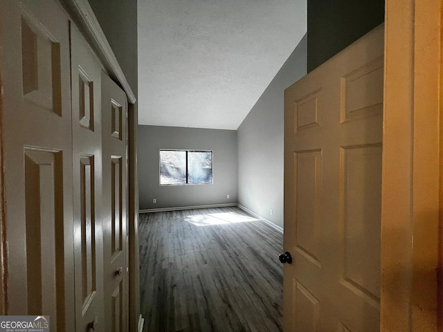 unfurnished bedroom with lofted ceiling, wood finished floors, baseboards, and a textured ceiling