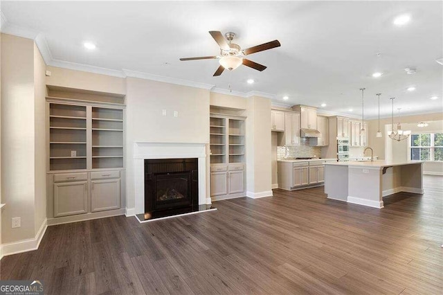 unfurnished living room with ornamental molding, sink, ceiling fan with notable chandelier, and hardwood / wood-style flooring