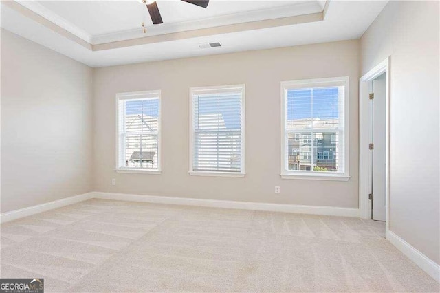 carpeted empty room with ceiling fan, a wealth of natural light, and a raised ceiling