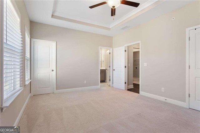 unfurnished bedroom featuring multiple windows, ceiling fan, a tray ceiling, and light colored carpet