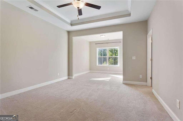 unfurnished room with a tray ceiling, light carpet, and ceiling fan