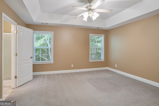 unfurnished bedroom featuring a raised ceiling, ceiling fan, and light carpet