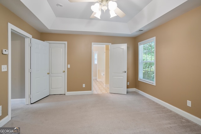 unfurnished bedroom featuring light carpet, a tray ceiling, and ceiling fan