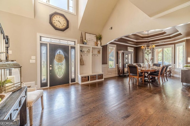 foyer with a high ceiling, ornamental molding, an inviting chandelier, dark hardwood / wood-style floors, and a tray ceiling