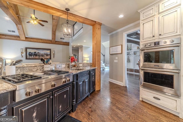 kitchen featuring dark hardwood / wood-style floors, ceiling fan with notable chandelier, appliances with stainless steel finishes, beam ceiling, and light stone counters