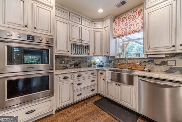 kitchen with sink, decorative backsplash, light stone countertops, dark hardwood / wood-style floors, and appliances with stainless steel finishes