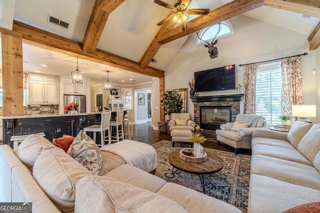 living room with beamed ceiling, ceiling fan with notable chandelier, a fireplace, dark wood-type flooring, and high vaulted ceiling