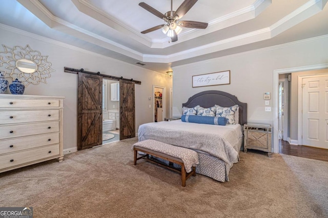 bedroom featuring a tray ceiling, connected bathroom, ornamental molding, a barn door, and ceiling fan