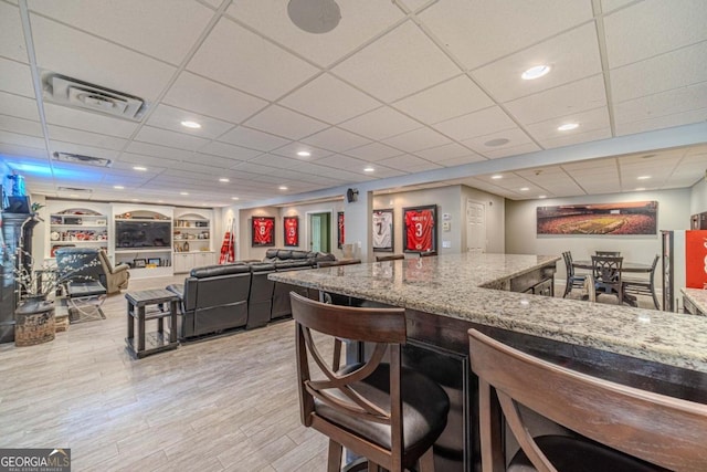 kitchen featuring a drop ceiling, light stone counters, a kitchen breakfast bar, and light hardwood / wood-style floors