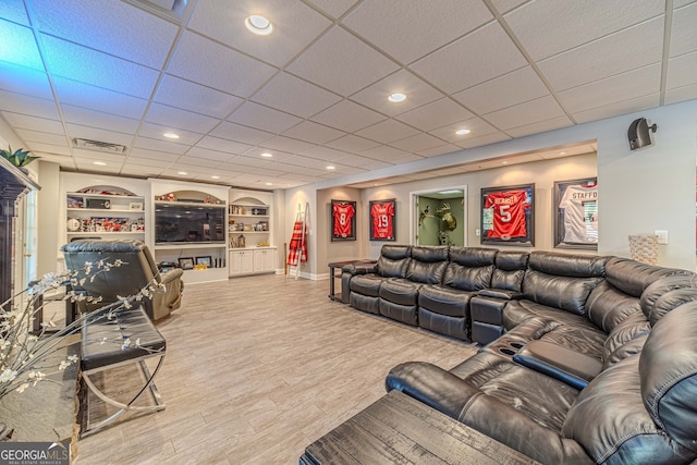 living room with built in shelves, wood-type flooring, and a paneled ceiling