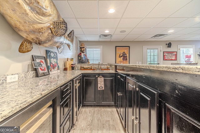 bar with a drop ceiling, light hardwood / wood-style flooring, light stone countertops, and a wealth of natural light