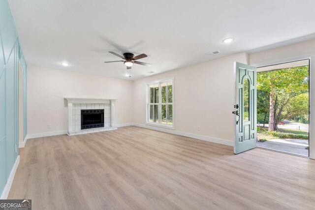 unfurnished living room with light wood-type flooring, ceiling fan, a tile fireplace, and a healthy amount of sunlight