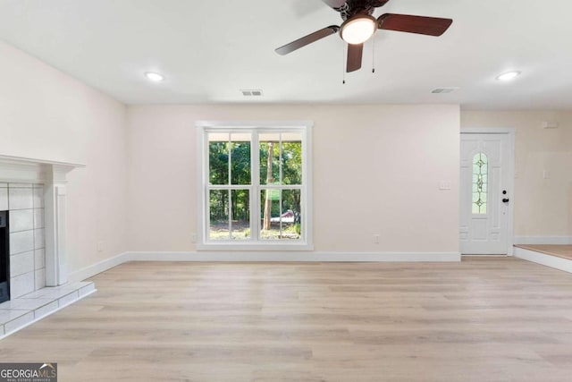 unfurnished living room featuring ceiling fan, light wood-type flooring, and a tile fireplace