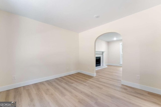 spare room featuring a brick fireplace and light hardwood / wood-style flooring