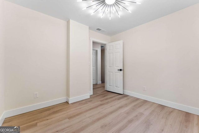 empty room featuring a notable chandelier and light hardwood / wood-style flooring