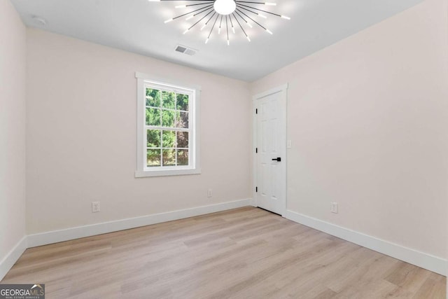 empty room featuring an inviting chandelier and light wood-type flooring