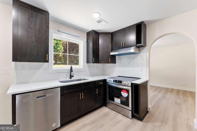 kitchen with tasteful backsplash, dark brown cabinets, stainless steel appliances, sink, and light hardwood / wood-style floors