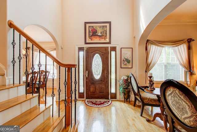 foyer with a high ceiling, ornamental molding, and light hardwood / wood-style flooring