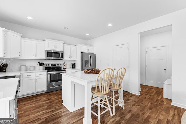321 Brown Station Dr, Williamson, GA 30292 - kitchen featuring white cabinets, appliances with stainless steel finishes, dark wood-style flooring, decorative backsplash, and a breakfast bar area