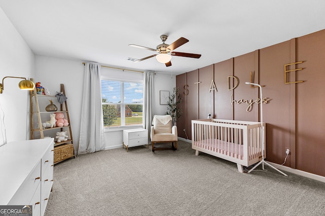 carpeted bedroom featuring ceiling fan and a crib