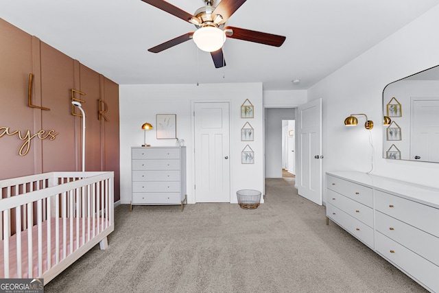 carpeted bedroom with a crib and ceiling fan