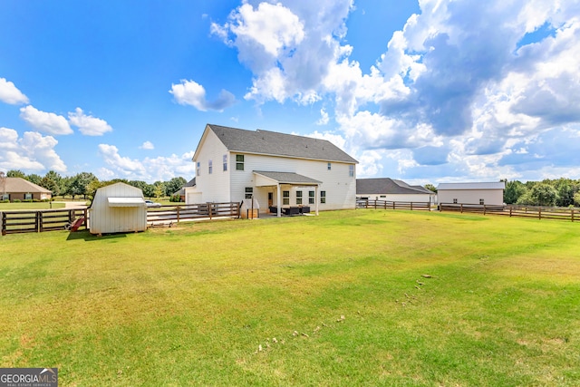 rear view of property featuring a lawn, a rural view, and a storage shed