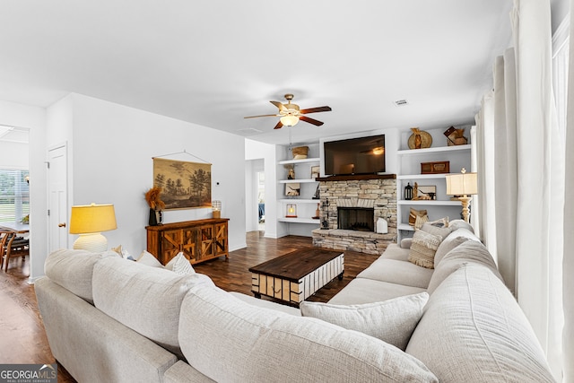 living room featuring built in features, wood-type flooring, ceiling fan, and a stone fireplace