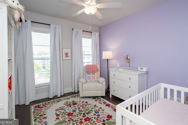 bedroom with ceiling fan, a nursery area, and dark hardwood / wood-style floors