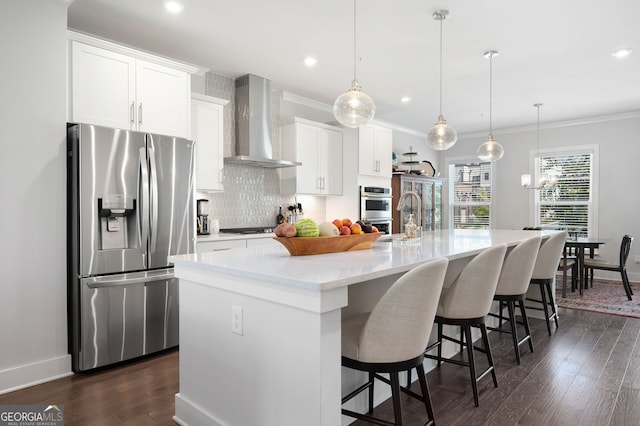 kitchen featuring dark wood-type flooring, an island with sink, hanging light fixtures, wall chimney exhaust hood, and stainless steel appliances