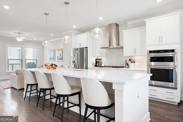 kitchen with a kitchen island with sink, stainless steel appliances, dark hardwood / wood-style floors, and wall chimney range hood