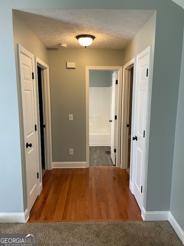 hall with a textured ceiling and dark hardwood / wood-style flooring