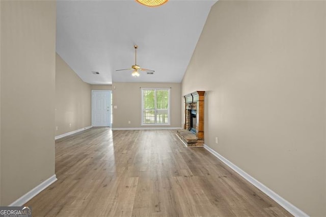 unfurnished living room featuring light wood-type flooring, ceiling fan, a stone fireplace, and vaulted ceiling