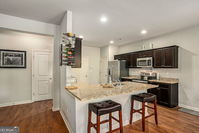 kitchen featuring appliances with stainless steel finishes, kitchen peninsula, a kitchen breakfast bar, and dark wood-type flooring