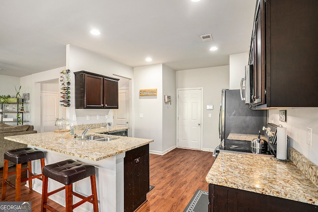 kitchen with a breakfast bar, sink, appliances with stainless steel finishes, dark brown cabinetry, and dark hardwood / wood-style flooring