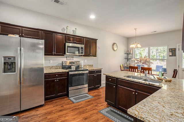 kitchen with appliances with stainless steel finishes, hanging light fixtures, light stone countertops, an inviting chandelier, and dark hardwood / wood-style floors