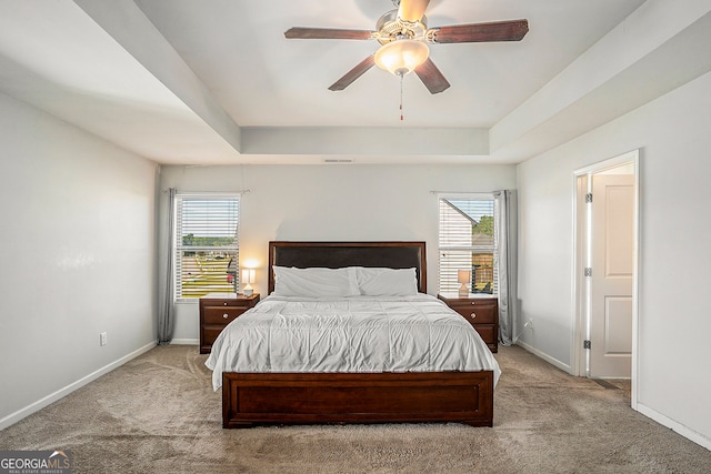 carpeted bedroom with multiple windows, a tray ceiling, and ceiling fan