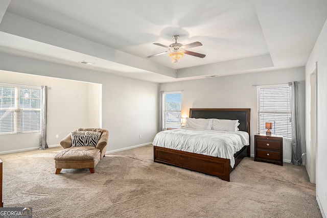 bedroom with ceiling fan, light colored carpet, a raised ceiling, and multiple windows