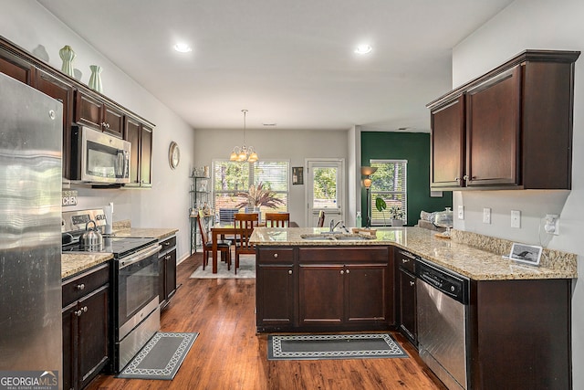 kitchen with kitchen peninsula, appliances with stainless steel finishes, hanging light fixtures, and dark hardwood / wood-style flooring