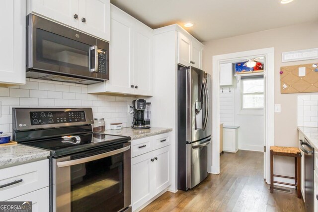 kitchen featuring white cabinets, light hardwood / wood-style flooring, light stone counters, stainless steel appliances, and tasteful backsplash