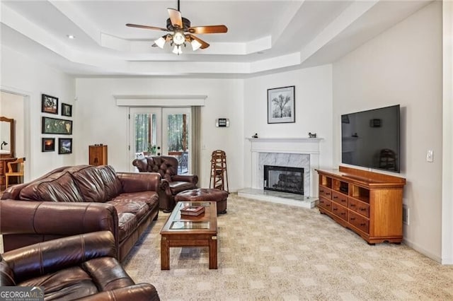 carpeted living room with a raised ceiling, a fireplace, ceiling fan, and french doors