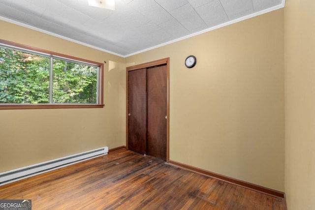 interior space featuring dark wood-type flooring, a baseboard heating unit, a closet, and crown molding