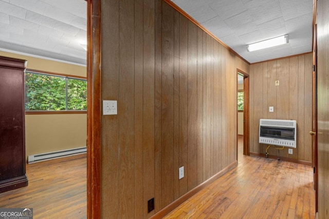 corridor with crown molding, wood walls, heating unit, a baseboard radiator, and light hardwood / wood-style floors