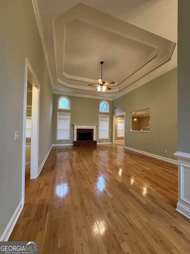 unfurnished living room featuring ornamental molding, a raised ceiling, ceiling fan, a fireplace, and light hardwood / wood-style floors